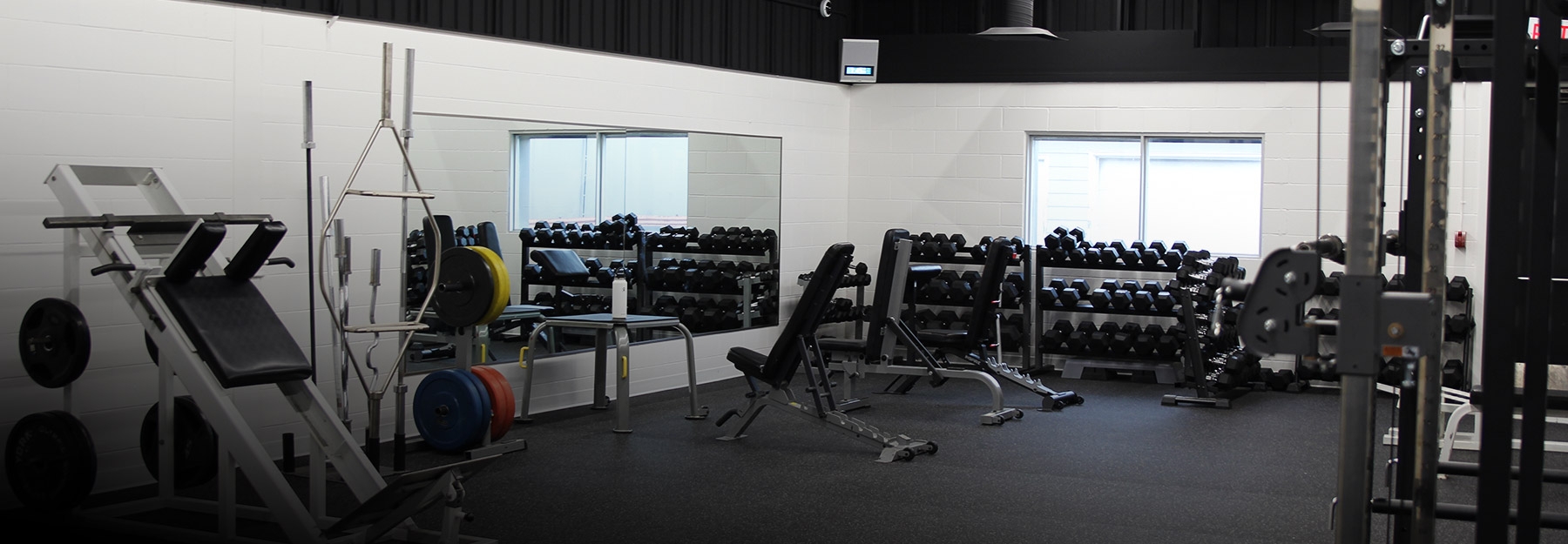 Fitness Centre with weight lifting equipment positioned along white walls with mirrors and windows.